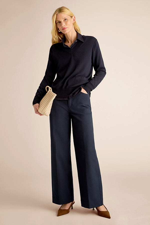 Woman wearing a black shirt and navy pants holding a woven handbag on a beige background | Exclude