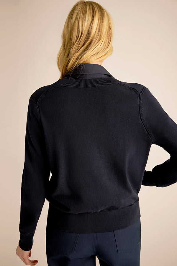 Person wearing a dark blue sweater and pants against a beige background | Exclude