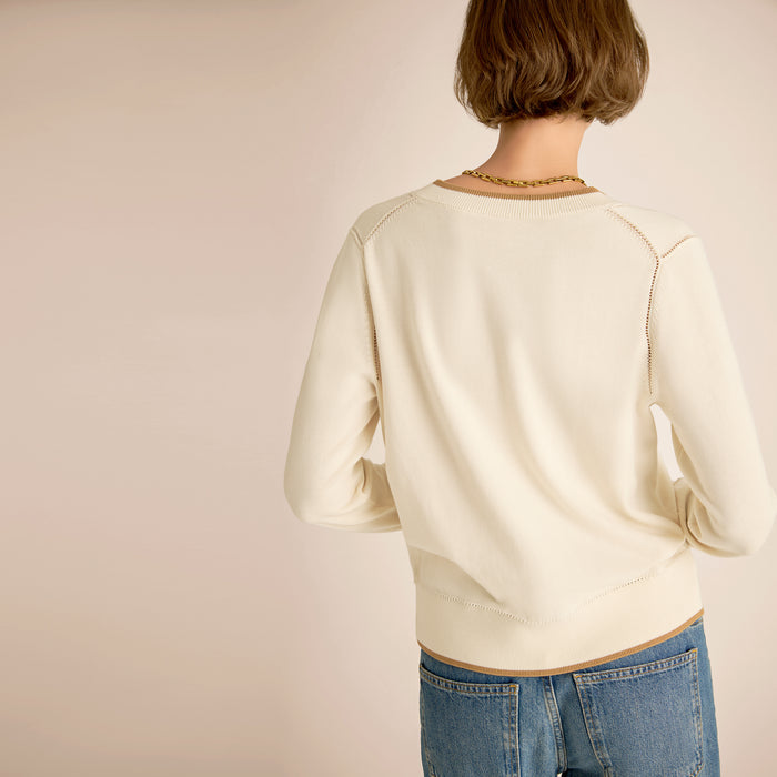 Person wearing a cream sweater and blue jeans on a plain background
