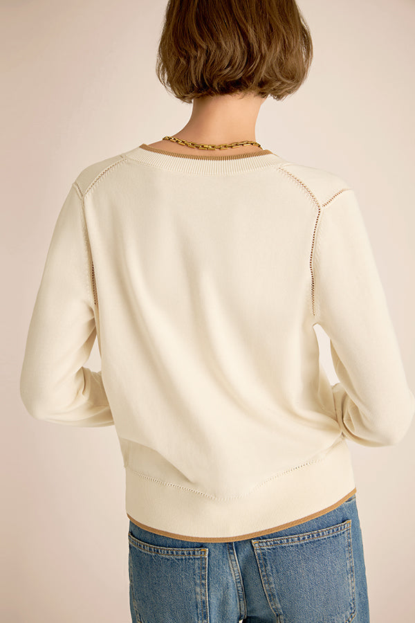 Person wearing a cream sweater and blue jeans on a plain background | Exclude