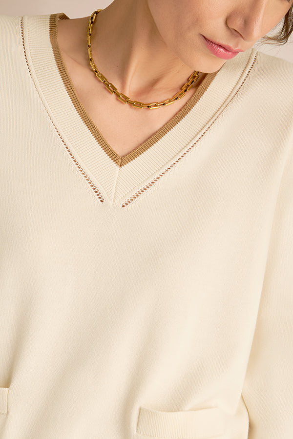 Close-up of a person wearing a cream-colored sweater with a gold chain necklace. | Exclude | Grid Hover