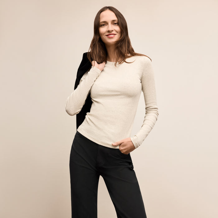 Woman wearing a beige sweater and black pants against a plain background  Lead