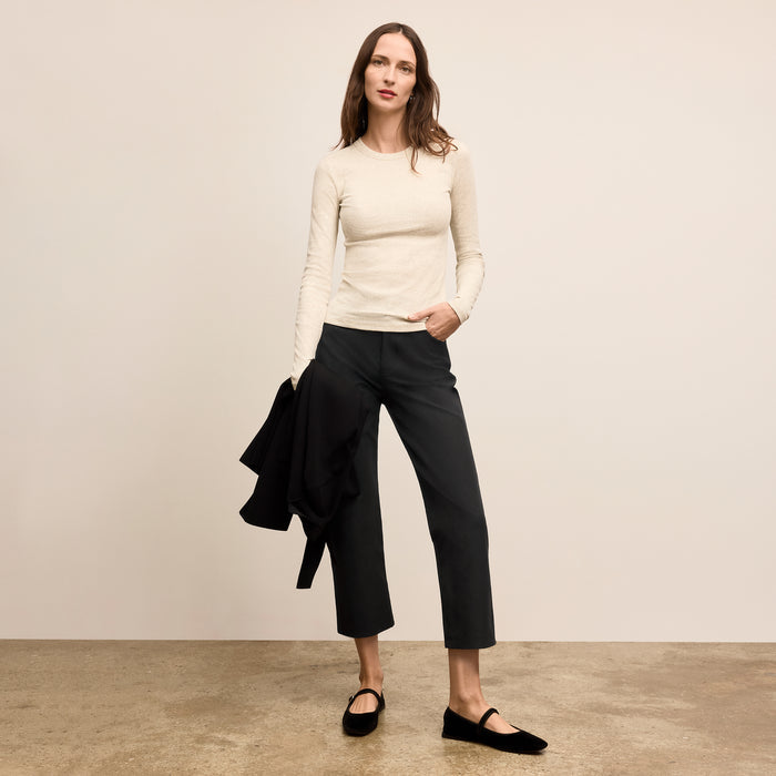 Woman wearing a cream sweater and black pants against a beige background