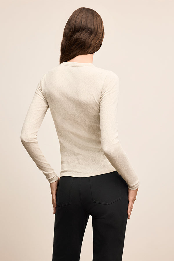 Person wearing a beige long-sleeve top and black pants on a beige background | Exclude
