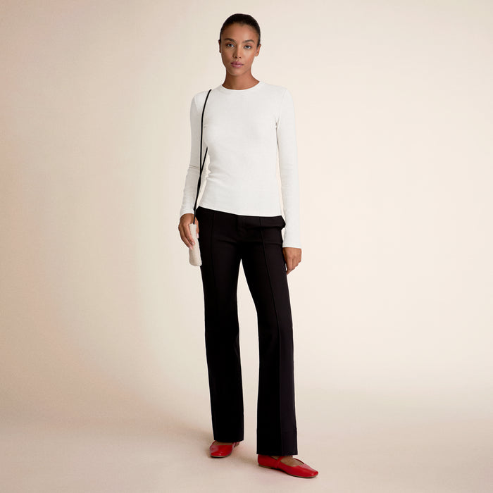 Woman wearing a white long-sleeve top, black pants, and red shoes on a beige background | Lead