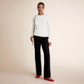 Woman wearing a white long-sleeve top, black pants, and red shoes on a beige background | Lead