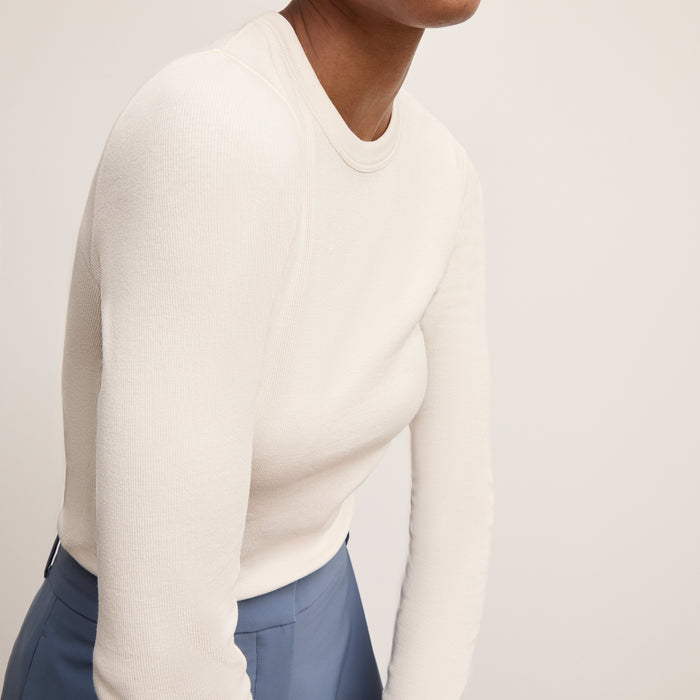 Person wearing a white sweater and blue pants on a plain background