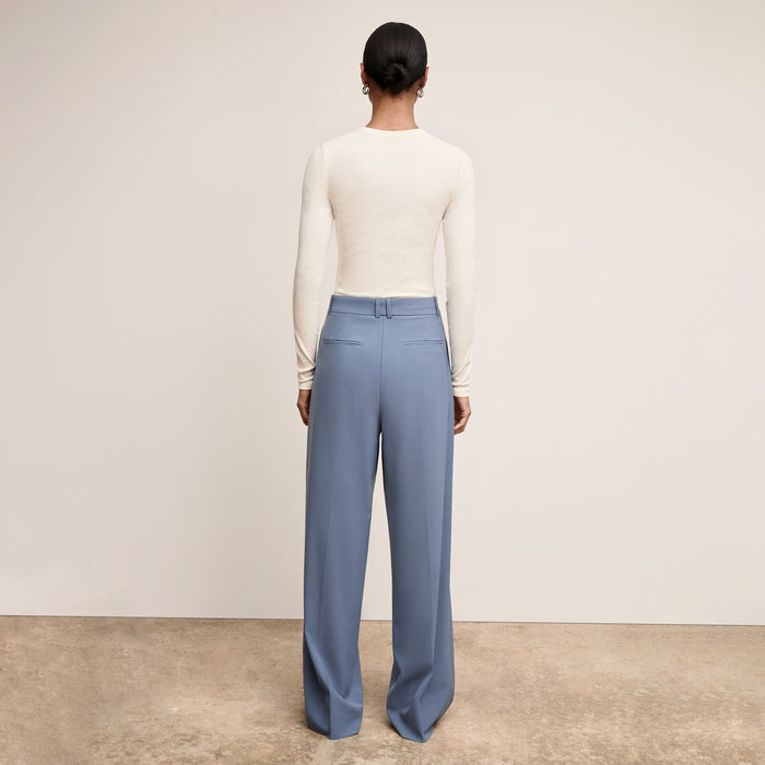 Woman wearing a white long-sleeve top and blue pants against a plain background