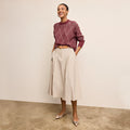 Woman wearing a maroon sweater and beige skirt against a plain background | Lead