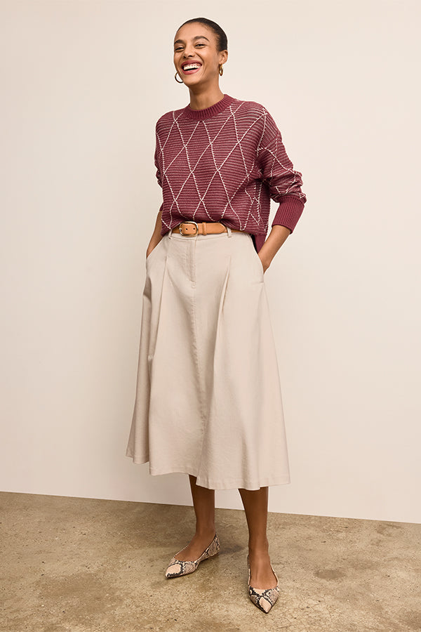 Woman wearing a burgundy sweater and beige skirt against a plain background | Exclude | Grid