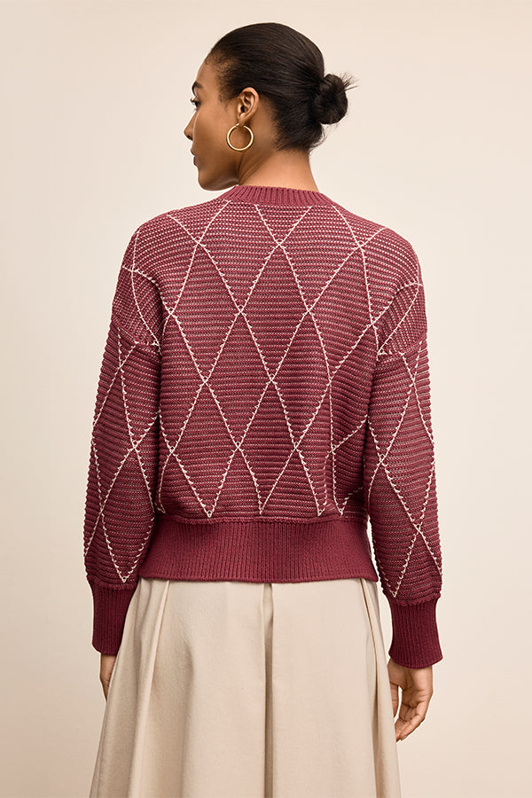 Woman wearing a maroon sweater with a geometric pattern on a beige background | Exclude