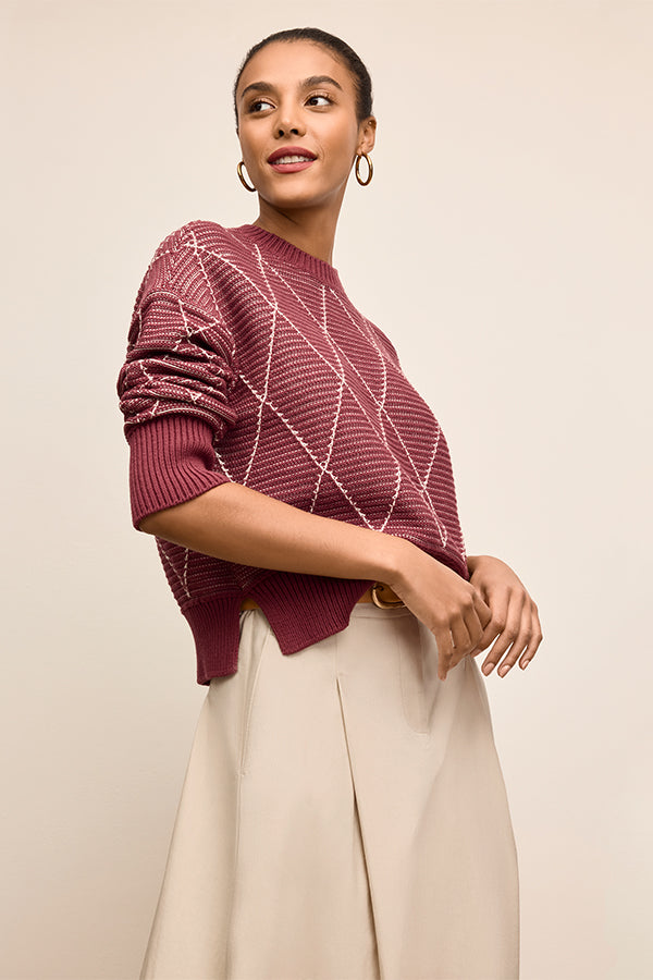 Woman wearing a maroon sweater with a geometric pattern on a beige background | Exclude | Grid Hover