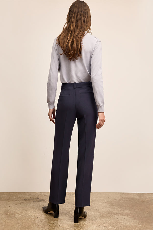 Person wearing a light gray shirt and dark blue pants against a beige background | Exclude