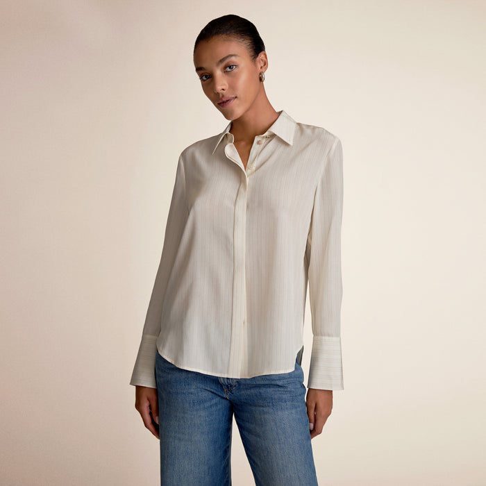 Woman wearing a light-colored shirt and blue jeans against a beige background | Lead
