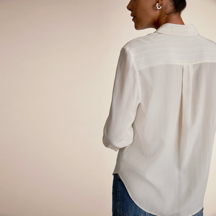 Person wearing a light-colored shirt and jeans against a plain background