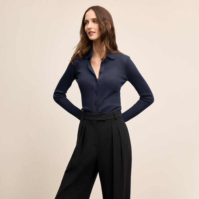 Woman wearing a navy blue shirt and black pants on a beige background | Lead