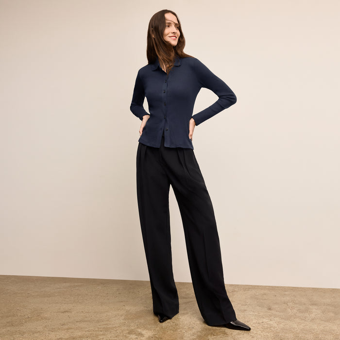 Woman wearing a navy blue shirt and black pants against a beige background