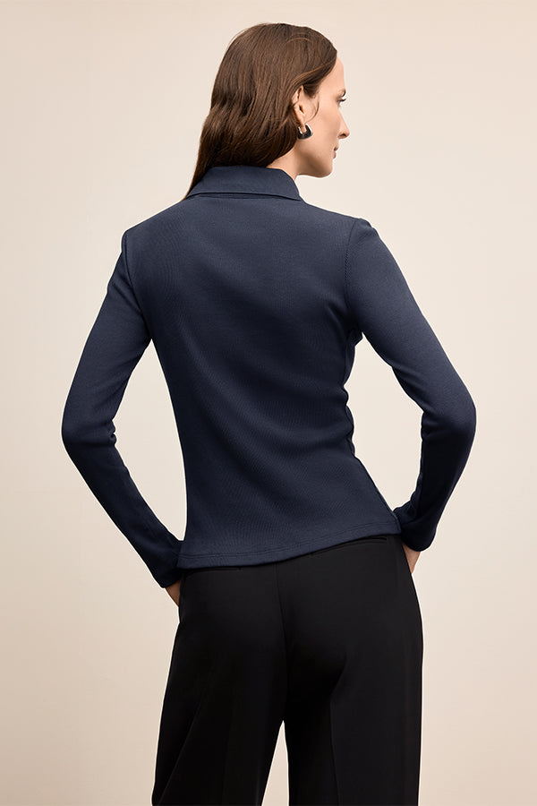 Woman wearing a navy blue long-sleeve top and black pants against a beige background | Exclude