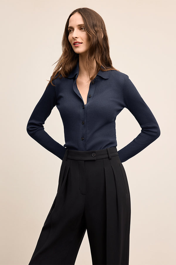 Woman wearing a navy blue shirt and black pants on a beige background | Exclude | Grid