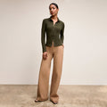 Woman wearing a green cardigan and beige pants against a neutral background | Lead