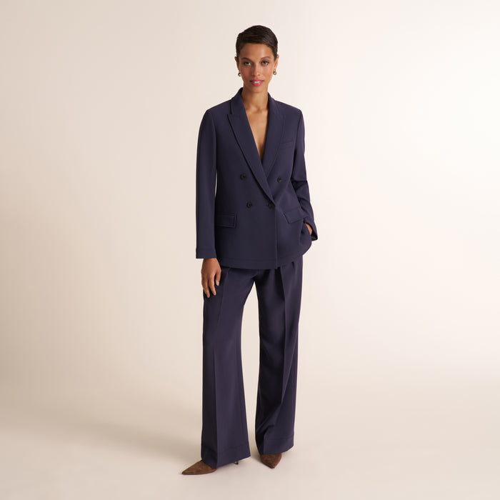 Woman wearing a navy and white knit tank top with navy pleated trouser pants and matching blazer | Lead