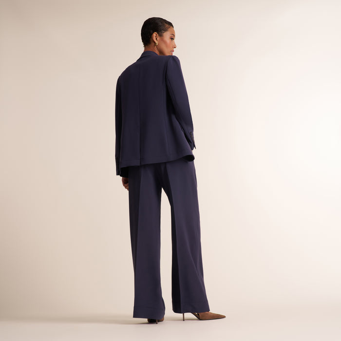 Woman wearing a navy and white knit tank top with navy pleated trouser pants and matching blazer