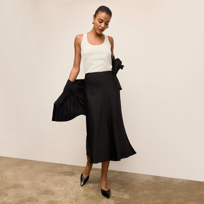 Woman wearing a white top and black skirt against a plain background | Lead