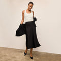 Woman wearing a white top and black skirt against a plain background | Lead