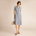 Woman wearing a blue patterned dress holding a straw bag on a beige background | Lead