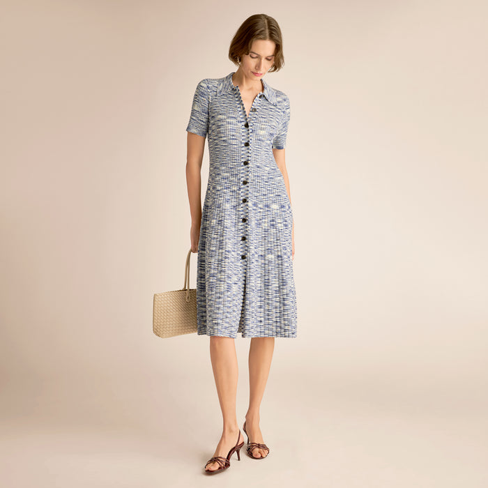 Woman wearing a blue patterned dress holding a straw bag on a beige background | Lead