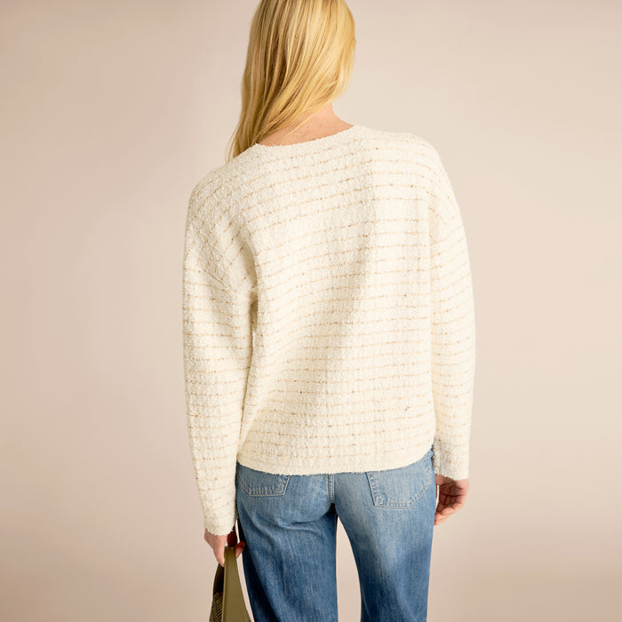 Person wearing a white textured sweater and blue jeans on a beige background