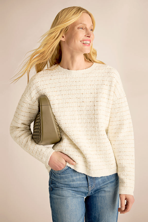 Woman wearing a cream sweater and blue jeans, holding a beige handbag against a plain background | Exclude | Grid