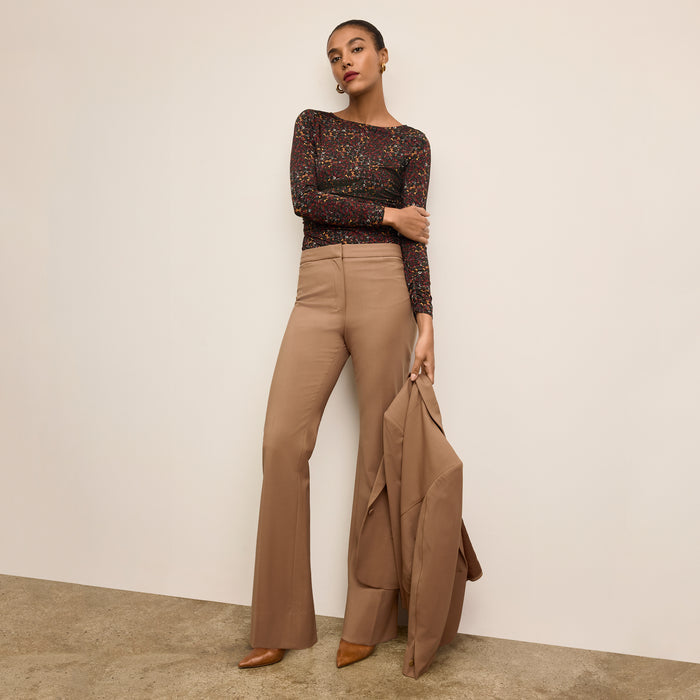 Woman wearing a patterned top and beige pants holding a matching jacket against a neutral background