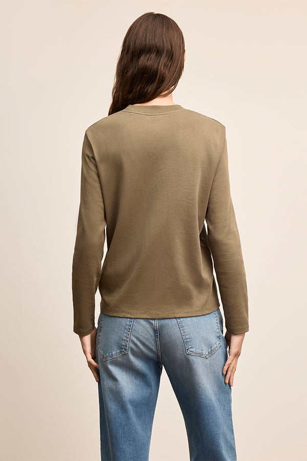 Person wearing a brown long-sleeve shirt and blue jeans on a beige background | Exclude | Grid Hover