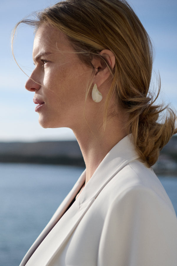 Woman with a ponytail wearing earrings by the water | Exclude | Grid Hover
