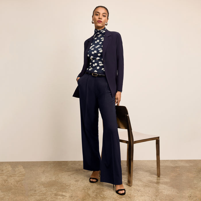 Woman wearing a navy suit with a floral blouse against a beige background | Lead