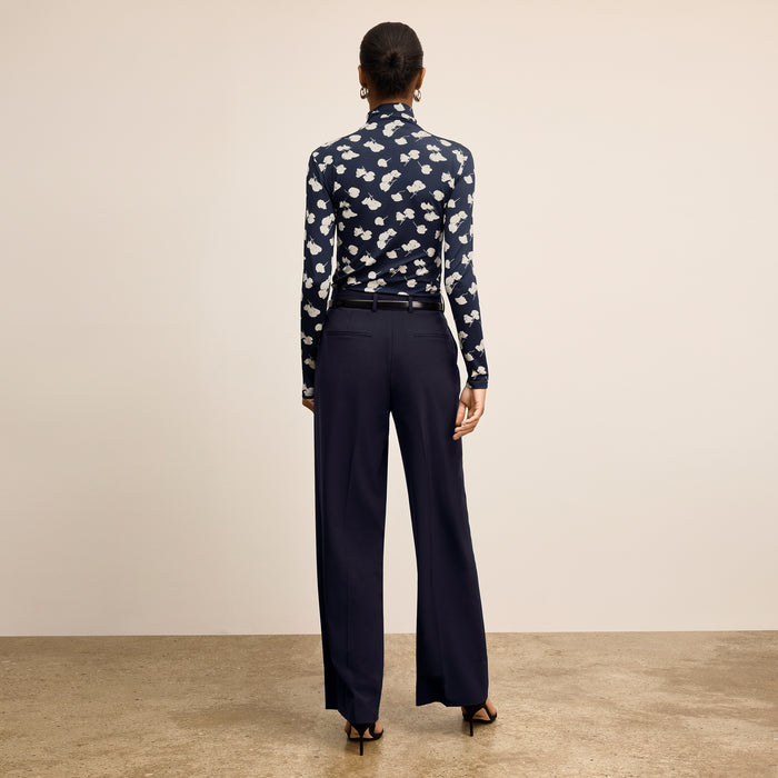 Woman wearing a navy patterned blouse and dark pants on a beige background