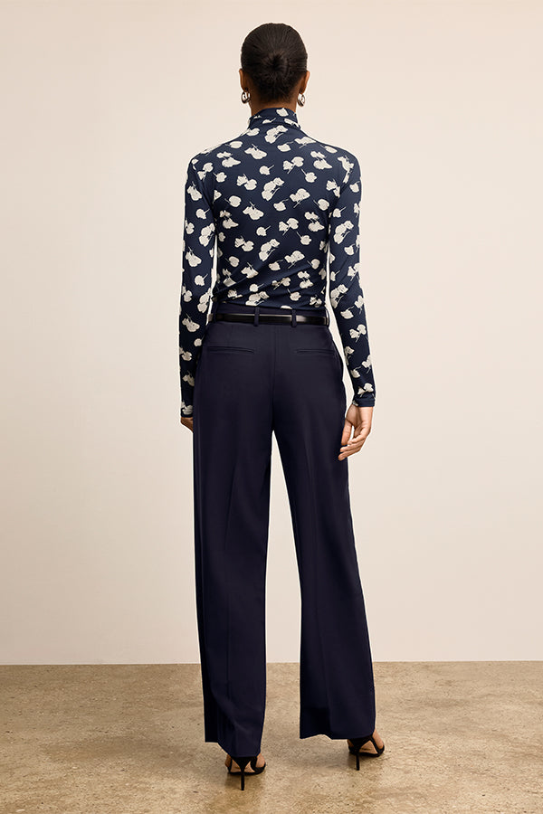 Woman wearing a navy patterned blouse and dark pants against a beige background | Exclude | Grid Hover