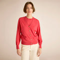 Woman wearing a red cardigan with gold buttons on a beige background | Lead