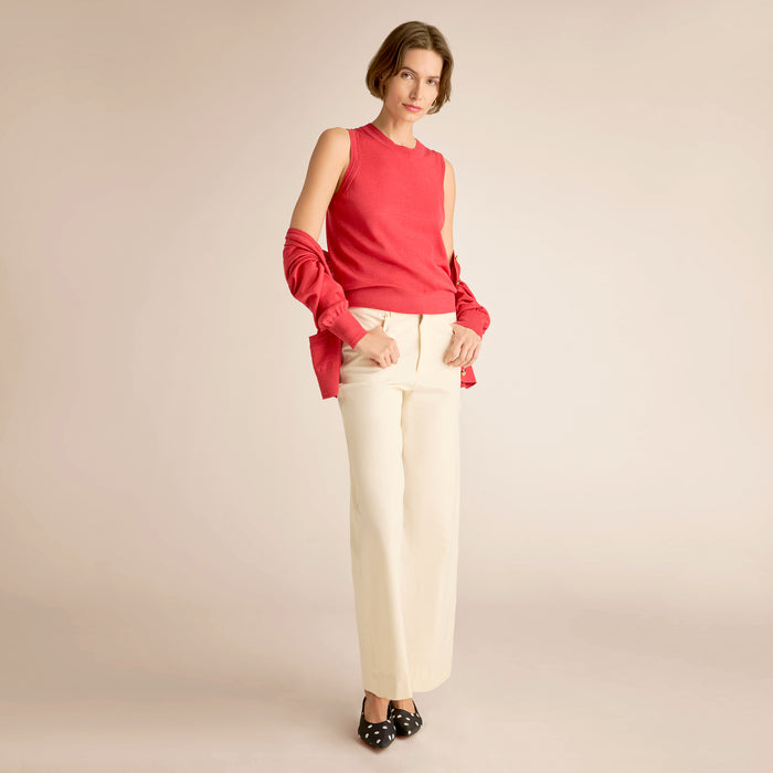 Woman wearing a red sleeveless top and white pants on a beige background