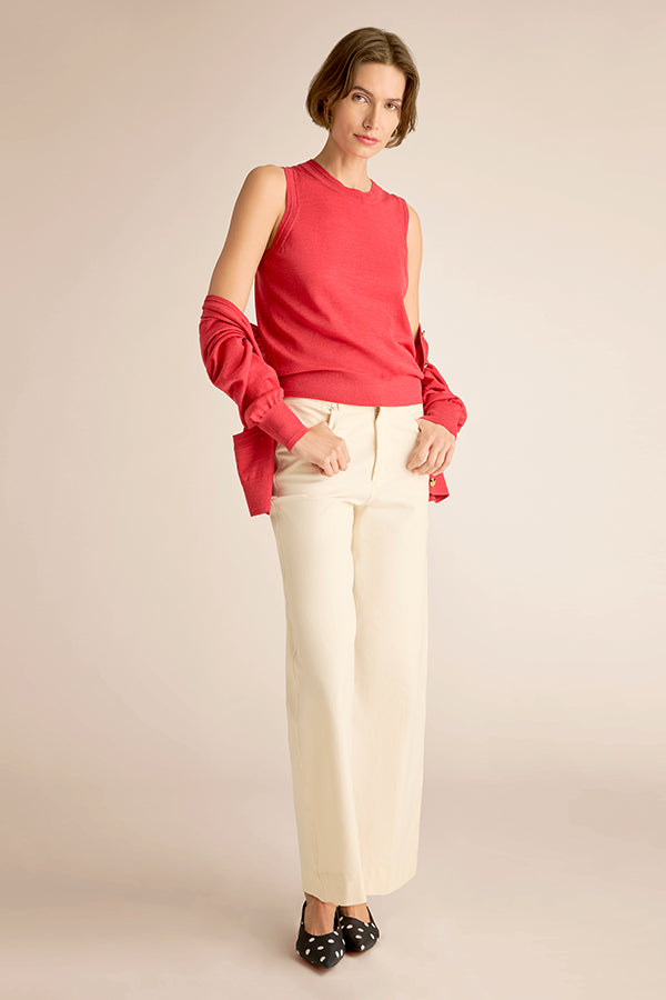 Woman wearing a red sleeveless top and white pants on a beige background | Exclude