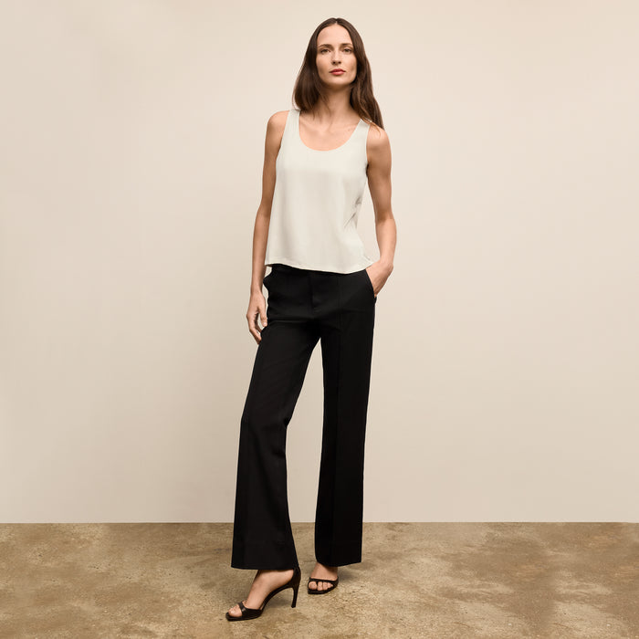 Woman wearing a white sleeveless top and black pants against a beige background | Lead