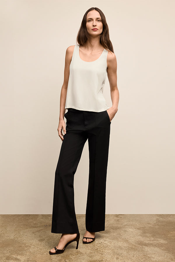 Woman wearing a white sleeveless top and black pants against a beige background | Exclude | Grid