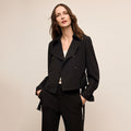 Woman wearing a black suit against a beige background | Lead