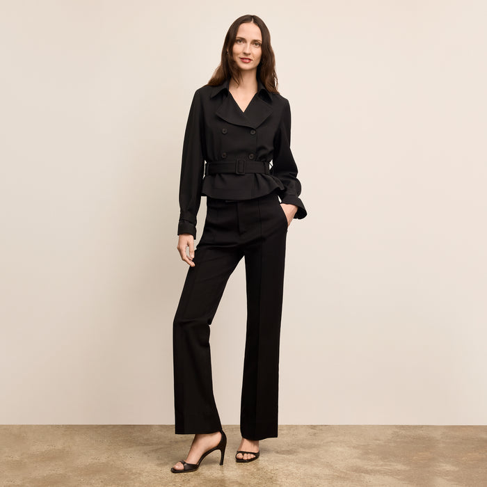 Woman wearing a black suit standing against a beige background