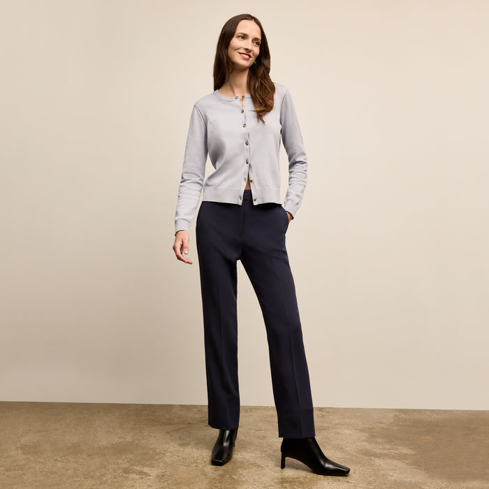 Woman wearing a light gray cardigan, black pants, and black shoes on a beige background | Lead
