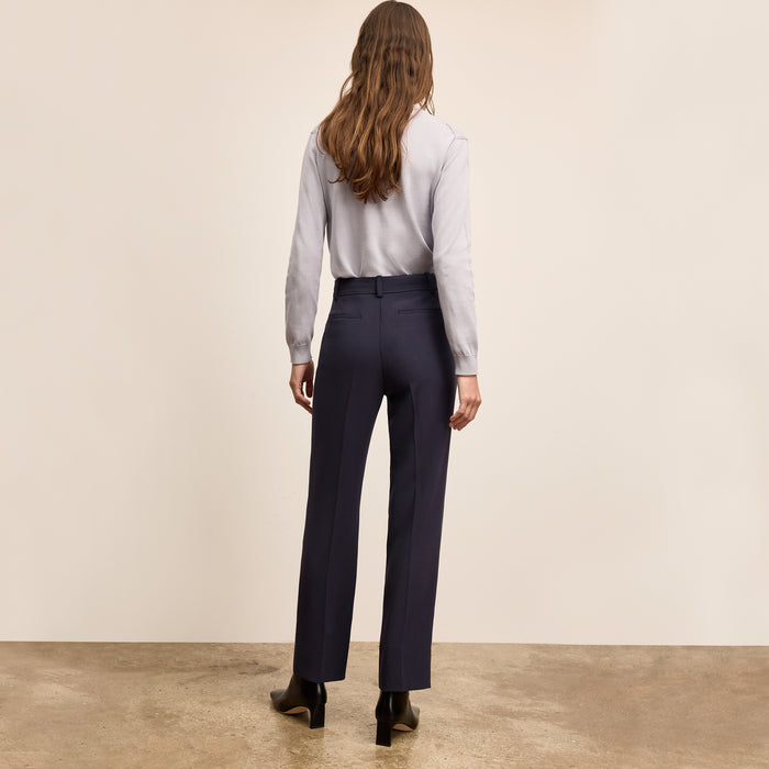 Person wearing a light gray shirt and dark blue pants against a beige wall.