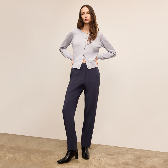 Woman wearing a light gray cardigan and dark blue pants against a beige background