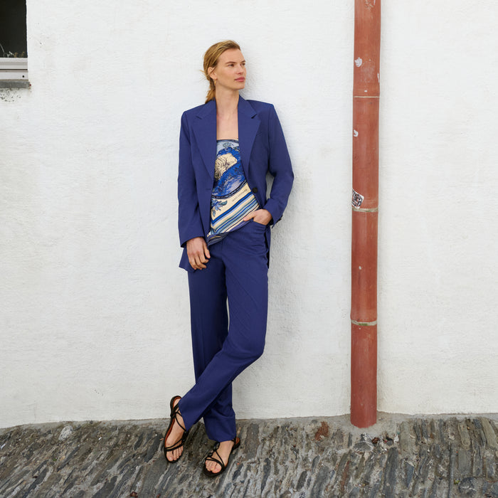 Woman in a blue suit standing against a white wall with a red cylindrical object.