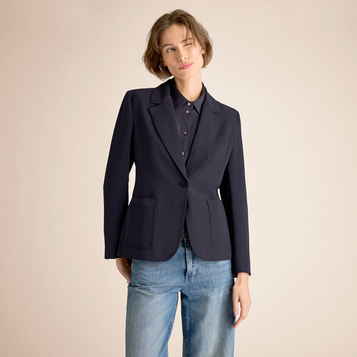 Person wearing a navy blazer over a shirt with light blue jeans on a beige background